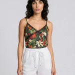 Woman wearing a tropical floral camisole with thin straps and white drawstring shorts, posed against a light gray background.