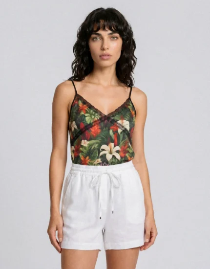 Woman wearing a tropical floral camisole with thin straps and white drawstring shorts, posed against a light gray background.